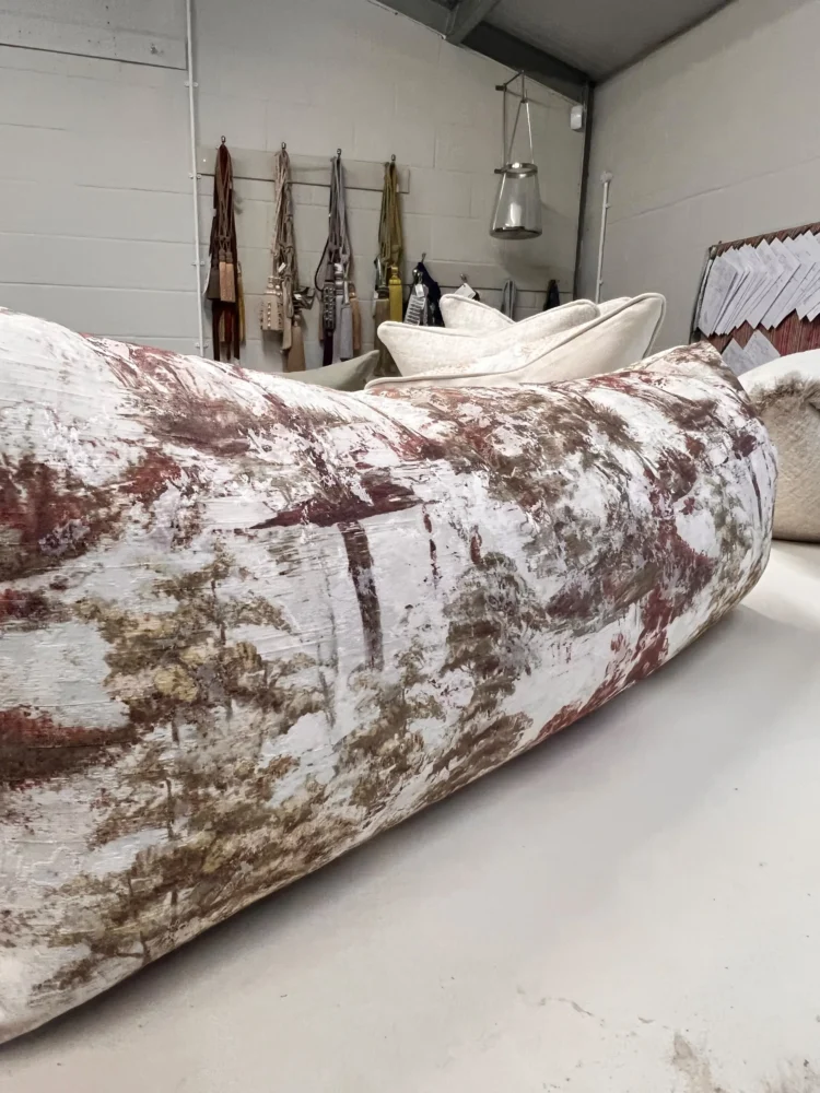 Long bolster cushion in a cream and rust abstract print, with fabric samples hanging on the workroom wall behind