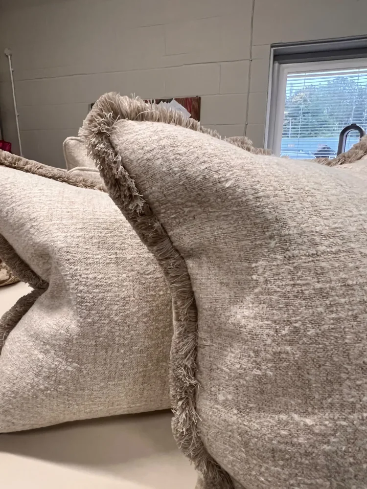 Neutral textured cushion with a fringed edge, close up beside a workroom window