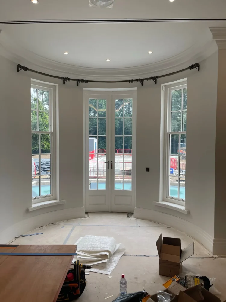Curved curtain pole fitted around a bay of sash windows and French doors, in a room still being finished