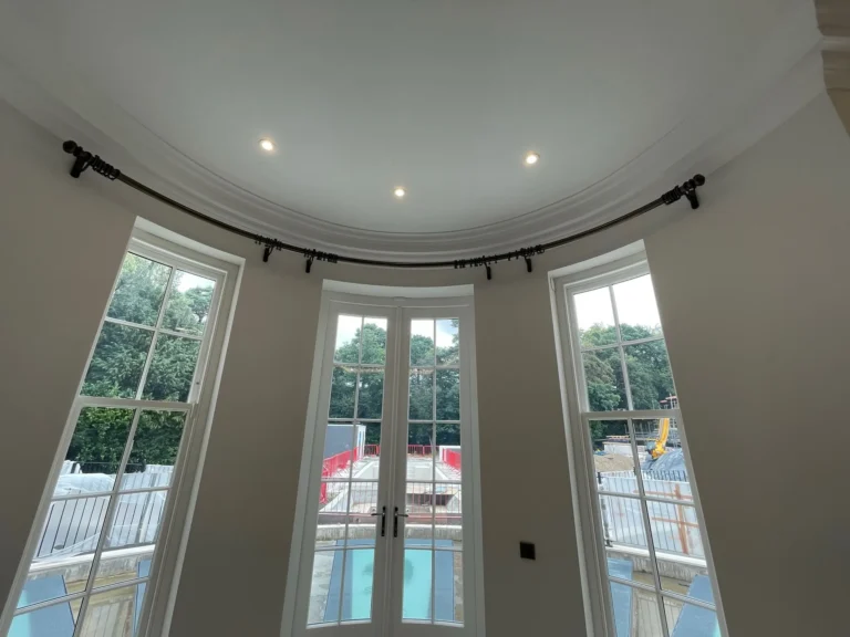 Looking up at a curved curtain pole around a bay with French doors, before the curtains were hung