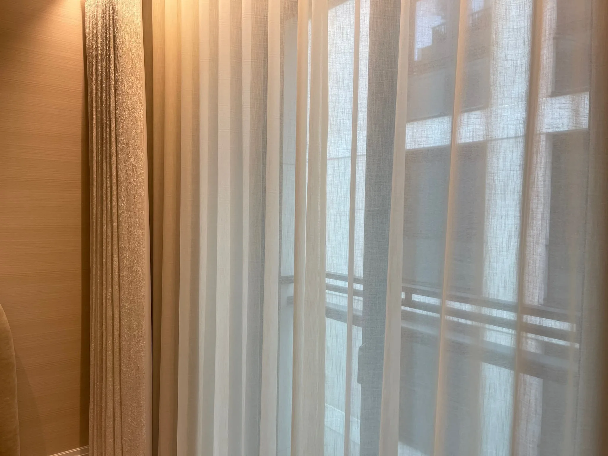 Sheer wave voiles backlit by tall windows, beside a wood-veneer wall with concealed lighting