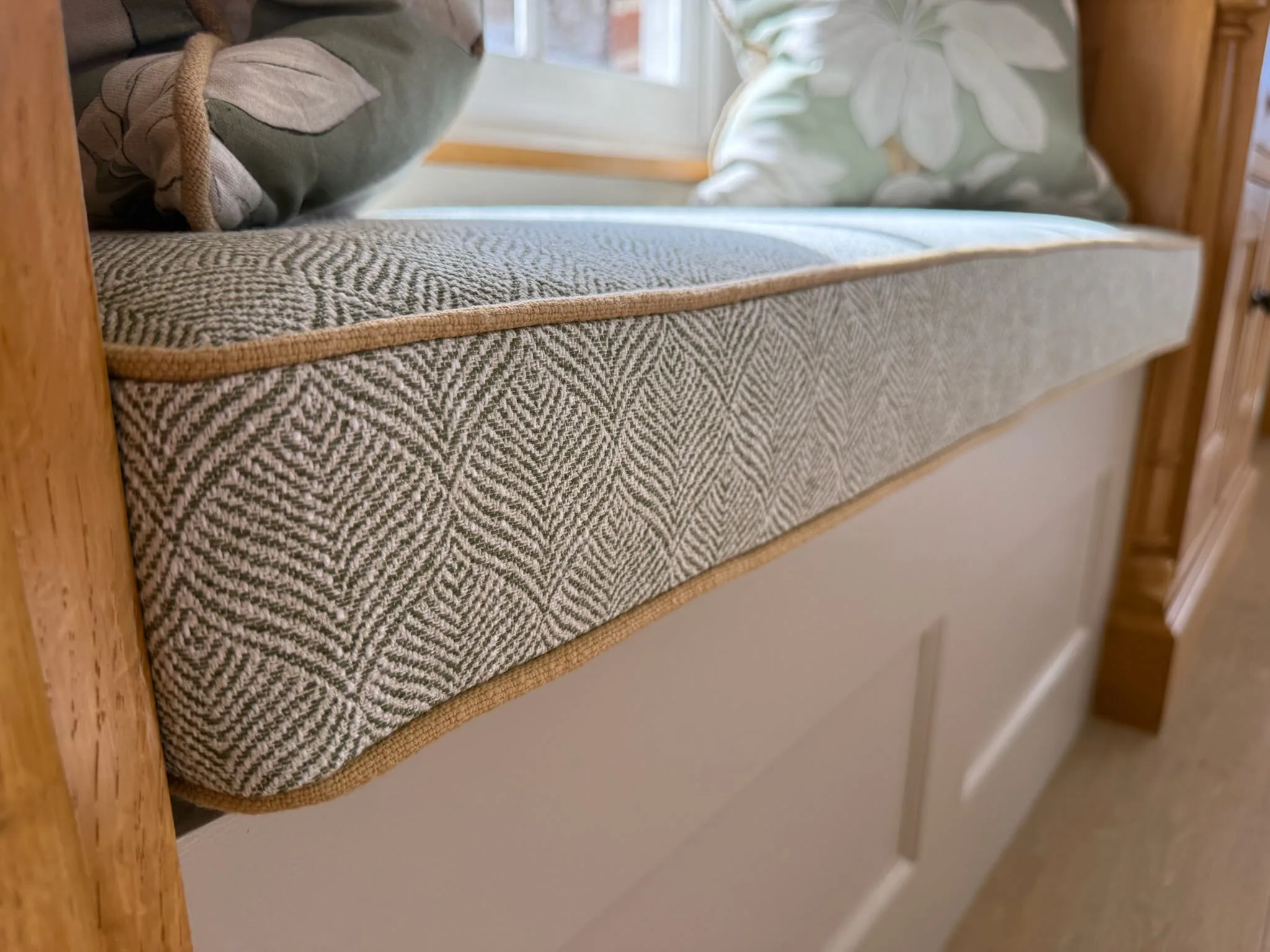 Piped window-seat cushion in a grey geometric weave, with leaf-print scatter cushions behind