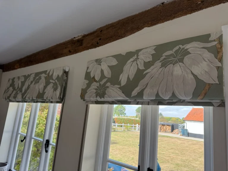Two Roman blinds in a large sage leaf print beneath an exposed oak beam over casement windows