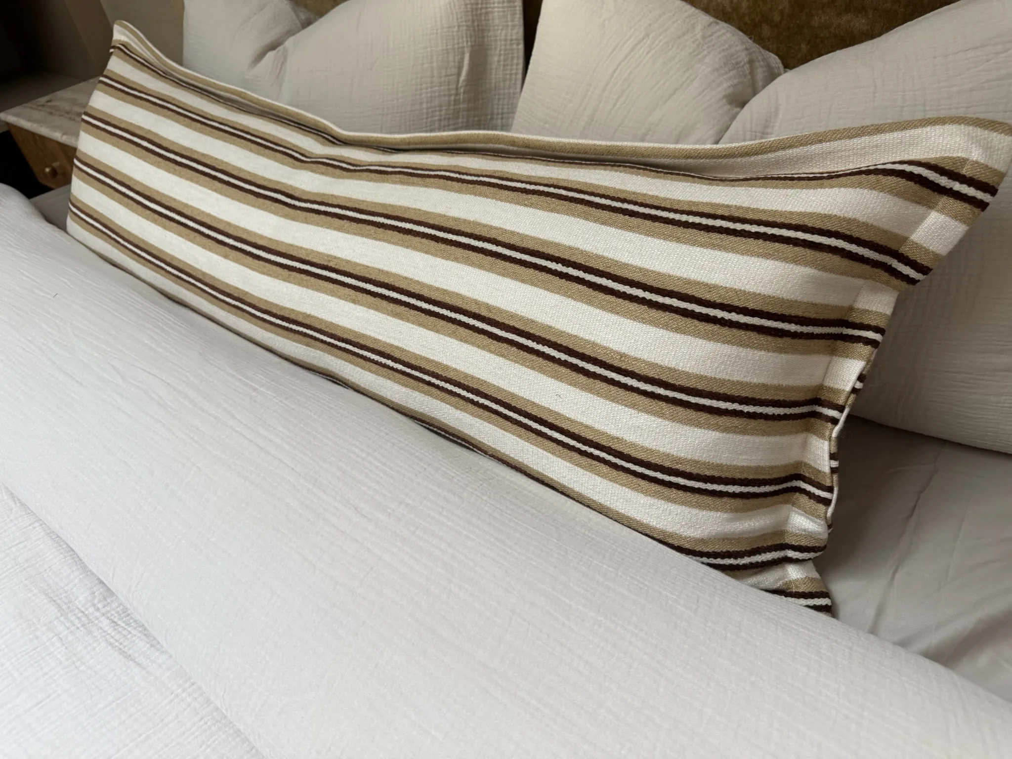 Striped bolster cushion in cream and brown laid on a white bed