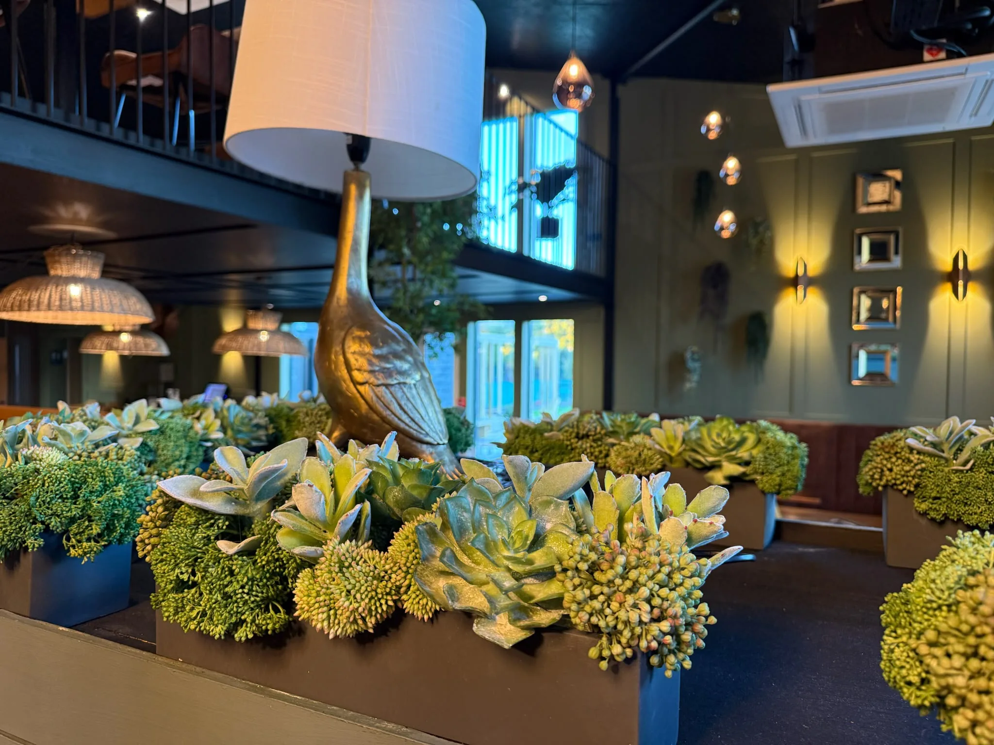 Restaurant interior with a brass bird table lamp above planted troughs and panelled walls with wall lights