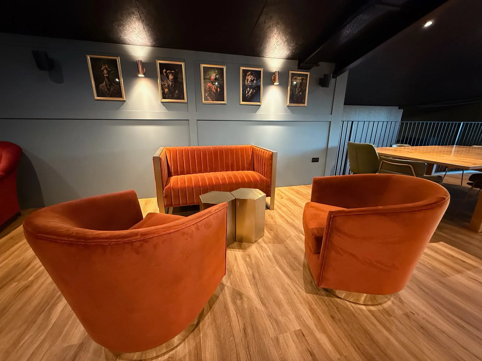 Lounge with three burnt-orange velvet tub chairs and a sofa around brass tables, beneath framed portraits