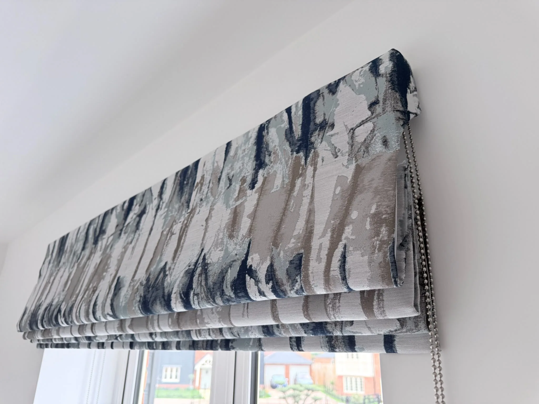 Roman blind in an abstract navy and grey print with a beaded chain, raised above a window