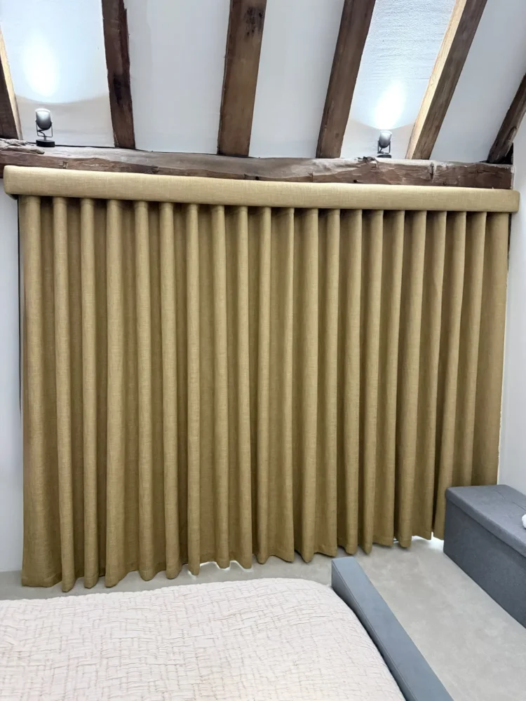 Mustard linen-look wave curtains on a ceiling track under exposed oak beams in a bedroom