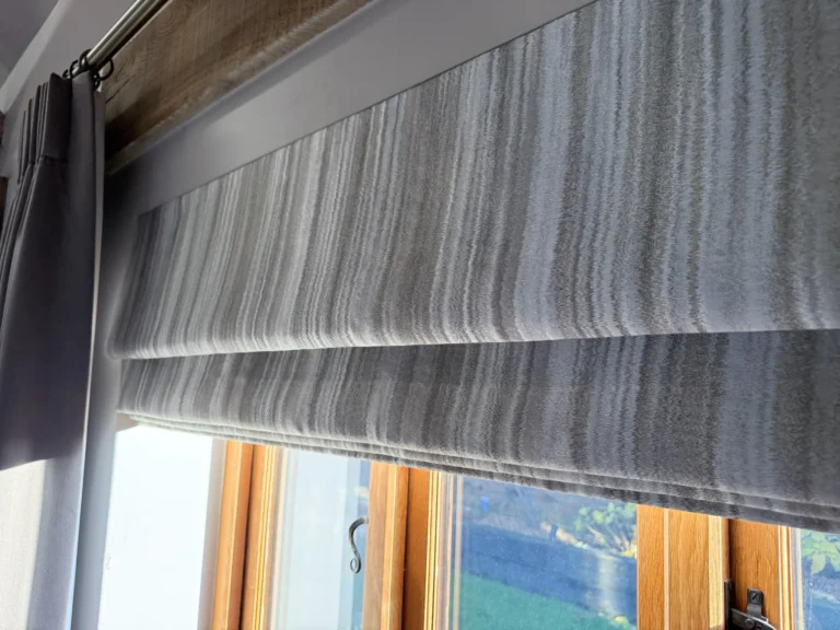 Close-up of a grey striped Roman blind raised in an oak-framed window, beside a grey curtain