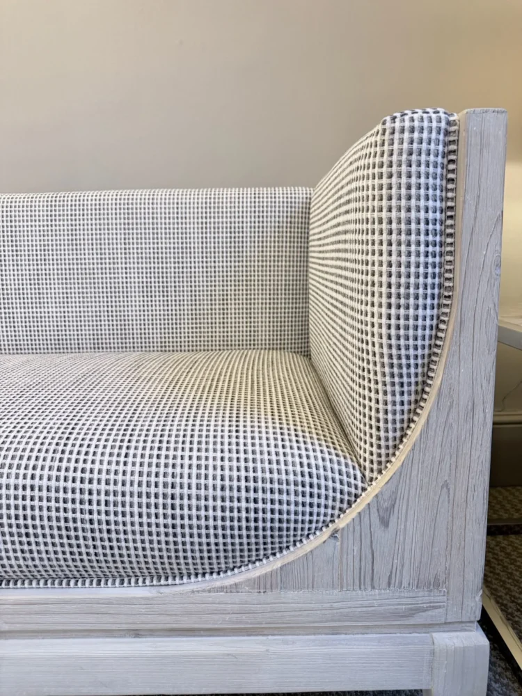 Close-up of a sofa end upholstered in a black and white check, with a pale oak frame