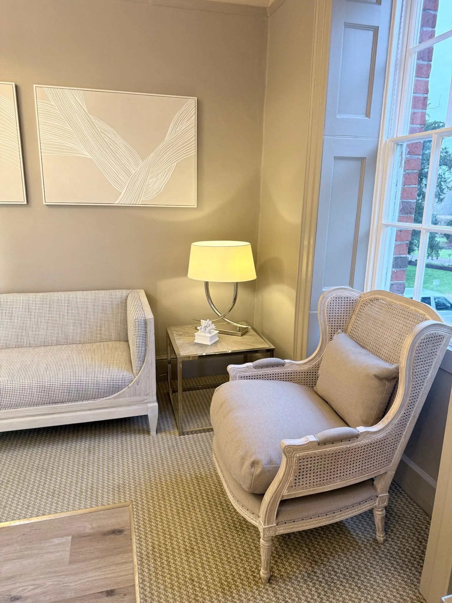 Waiting area in the Bridal Suite at Mulberry House, with an upholstered sofa, a cane-backed armchair and a lamp by a sash window