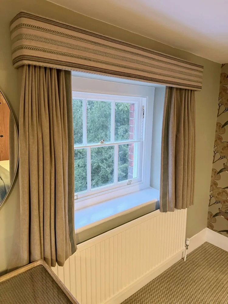 Striped box pelmet over full-length neutral curtains at a sash window, in a bedroom at Mulberry House