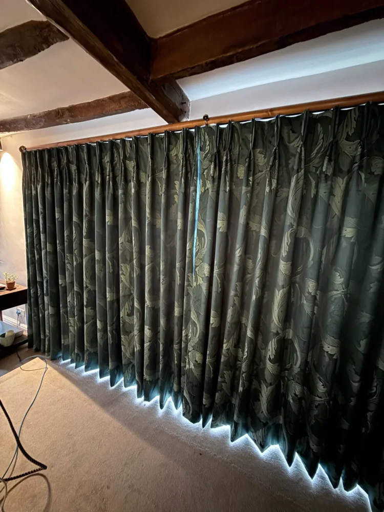 Dark green patterned pinch-pleat curtains drawn across a wide window under oak beams