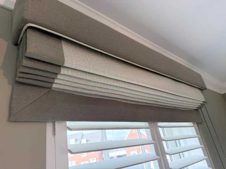 Neutral Roman blind with a contrast border, raised above window shutters