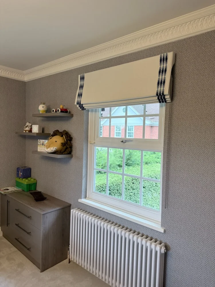 Neutral Roman blind with a black and white border at a sash window in a bedroom with toy shelves