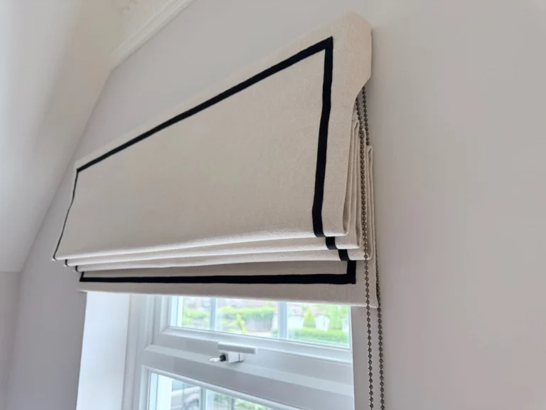 Neutral Roman blind with a black border, raised in a window set into a sloping ceiling