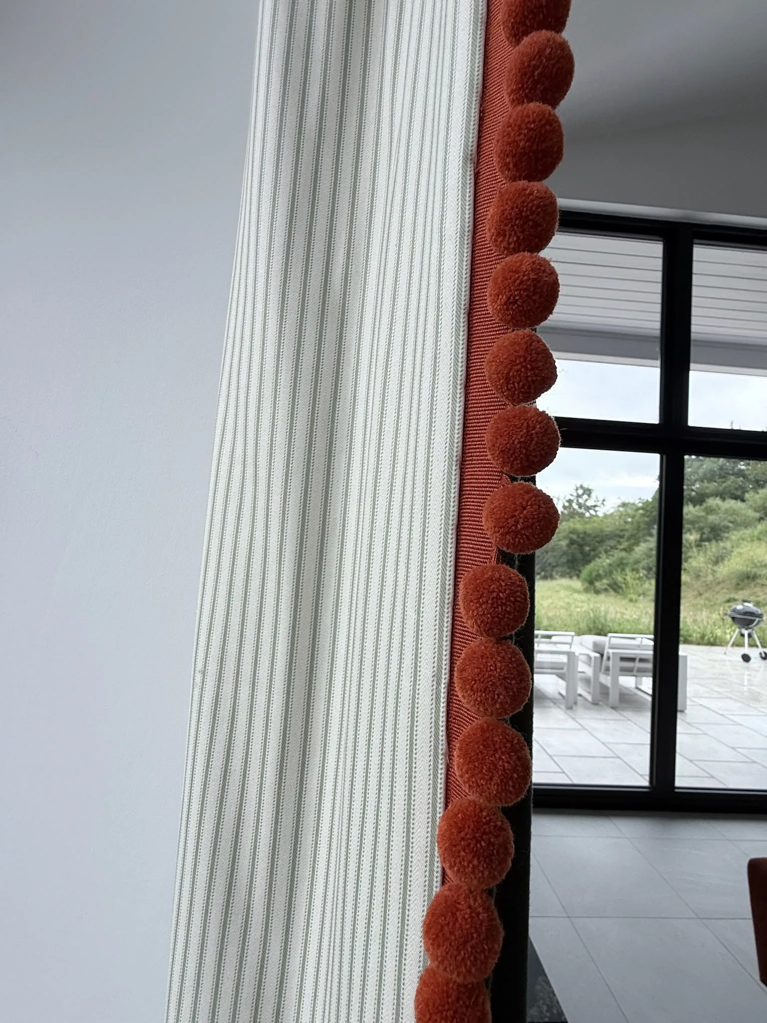 Striped curtain edged with an orange pom-pom trim beside black-framed glazing