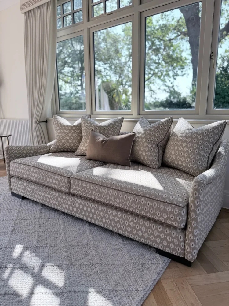 Three-seat sofa upholstered in a small geometric weave with matching scatter cushions, in front of tall windows