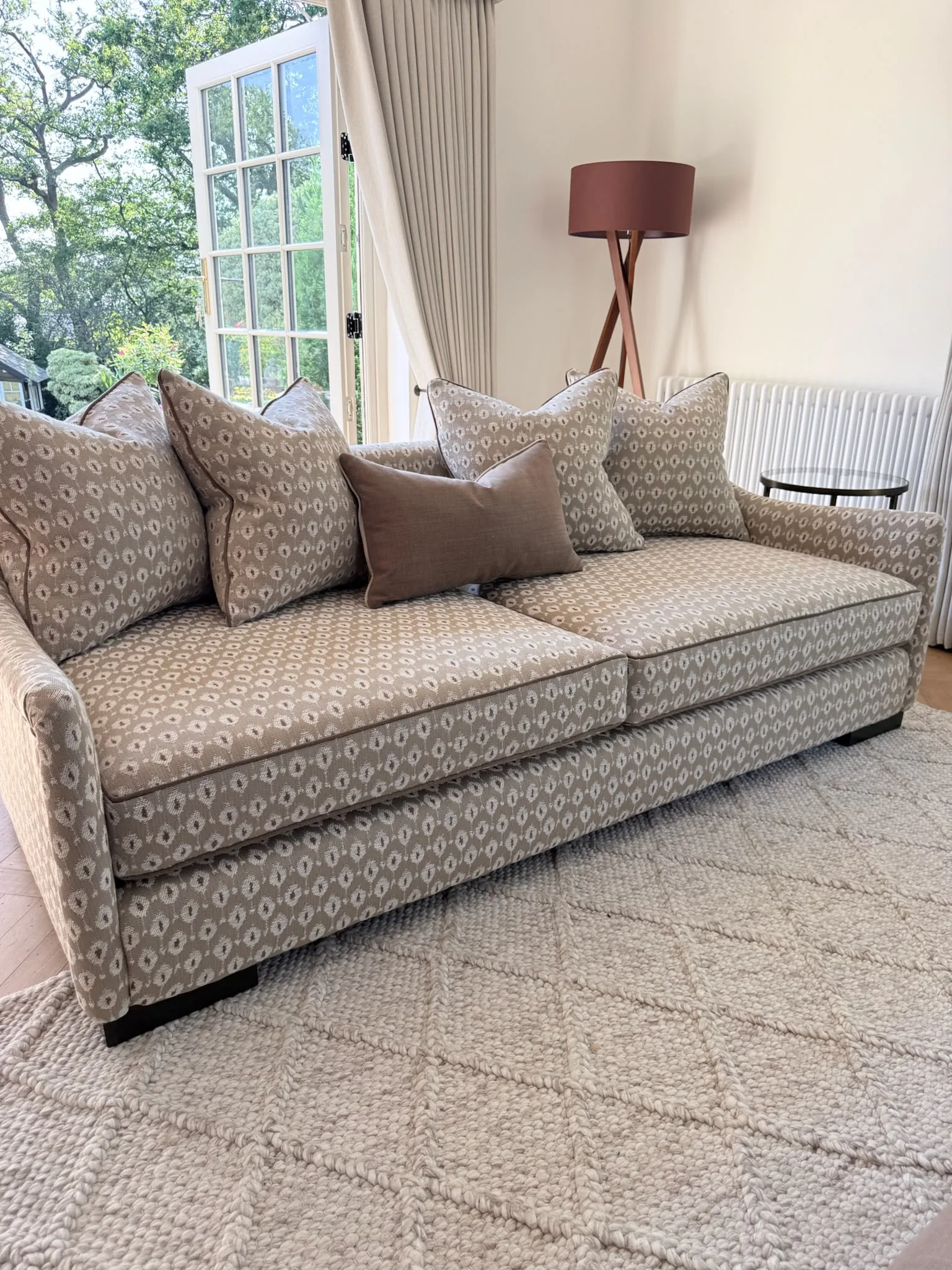 Sofa upholstered in a neutral geometric weave with patterned scatter cushions, beside French doors