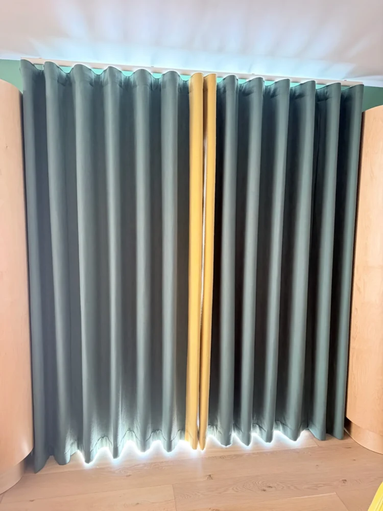 Teal wave curtains with a mustard edge on a ceiling track, with light showing at the hem