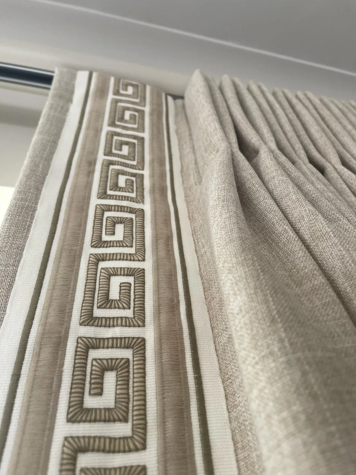 Close-up of a Greek key embroidered tape along the leading edge of neutral curtains