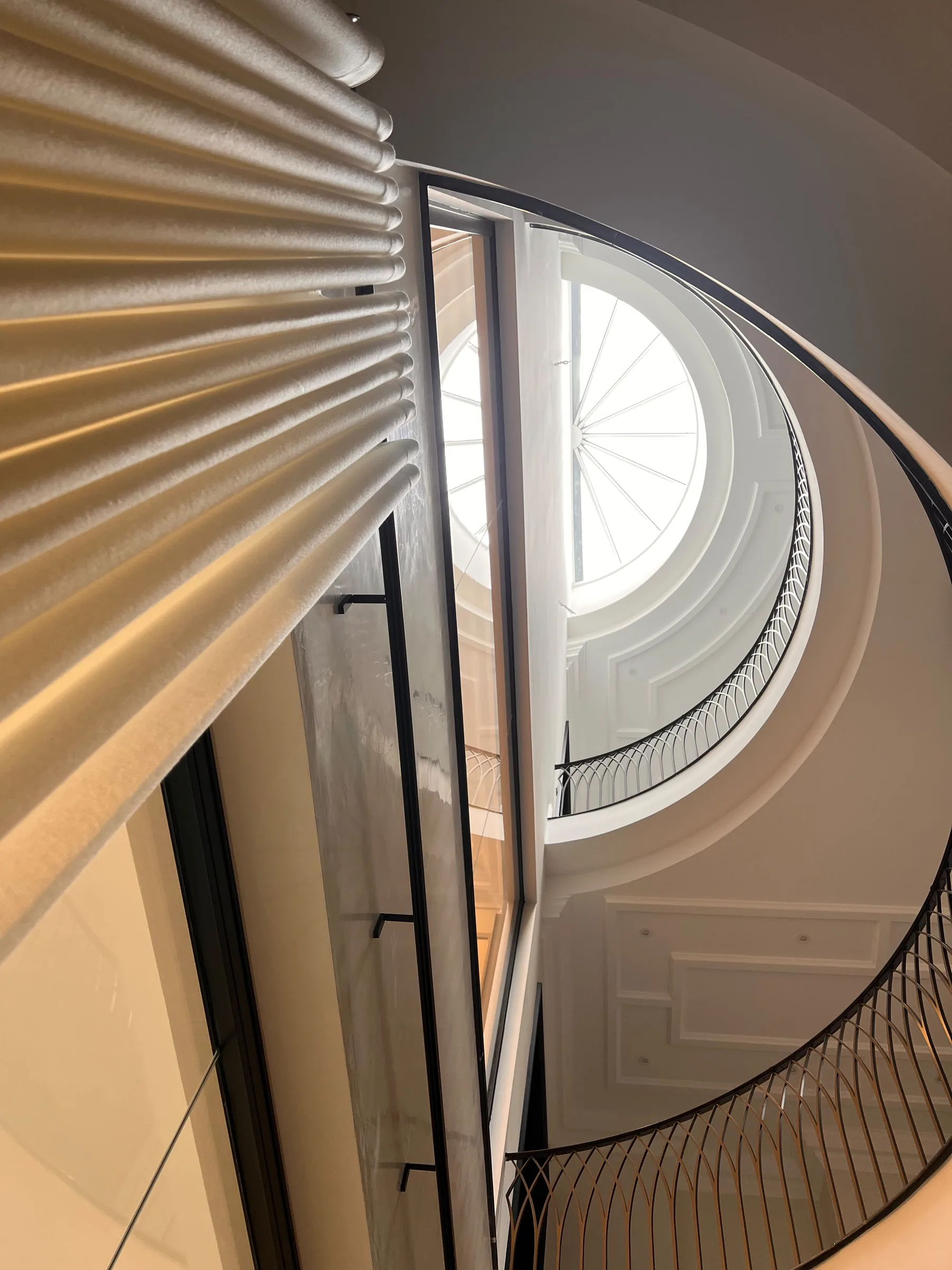 Looking up past a neutral wave curtain at a door towards a curved staircase and a round window