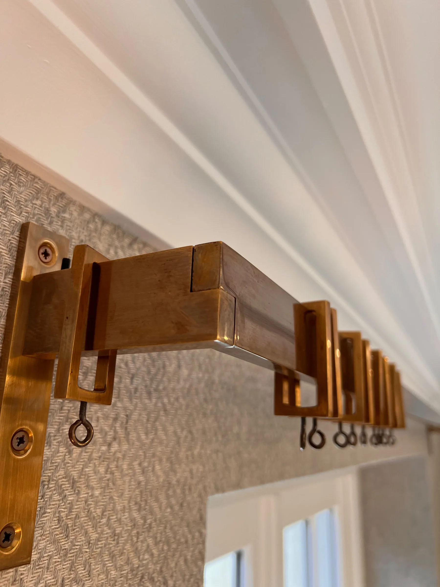 Square brass curtain pole and rings fitted against a textured wallcovering