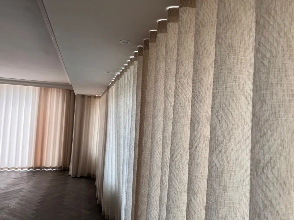 Long run of textured neutral wave curtains on a recessed ceiling track, along a room with a herringbone floor
