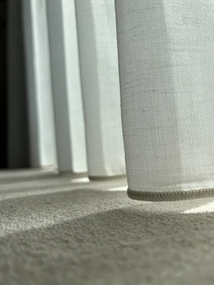 Close-up of the hem of a textured wave curtain just clearing a carpeted floor in sunlight