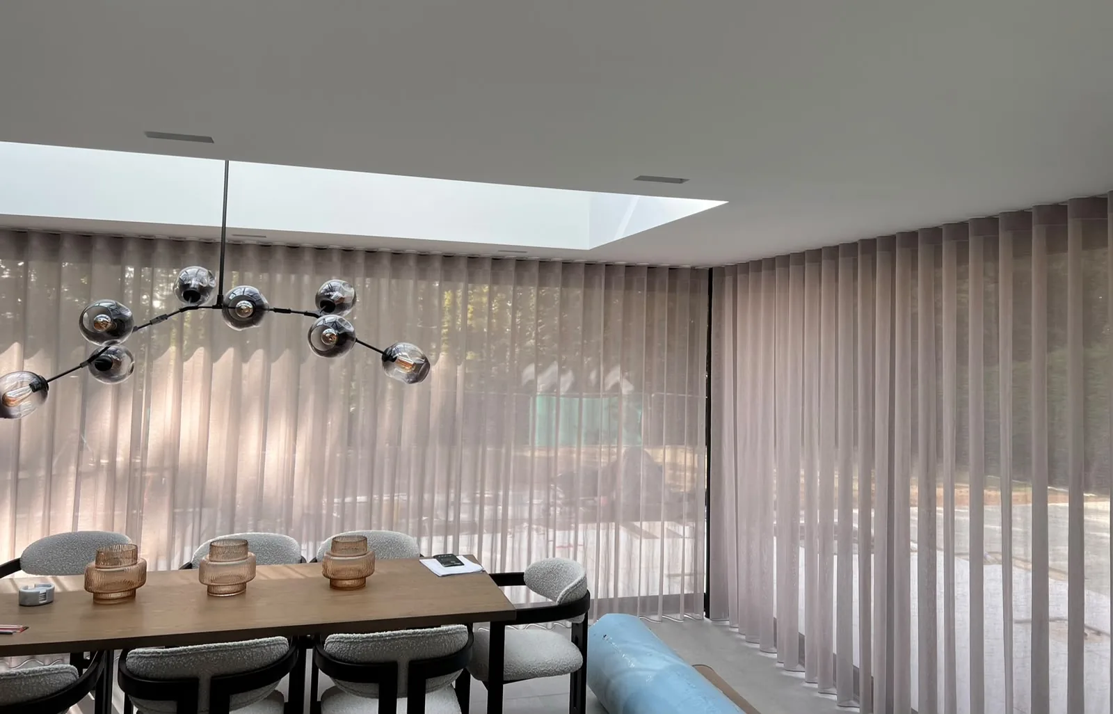 Dining area enclosed by floor-to-ceiling sheer wave voiles, with a rooflight and a branching glass pendant