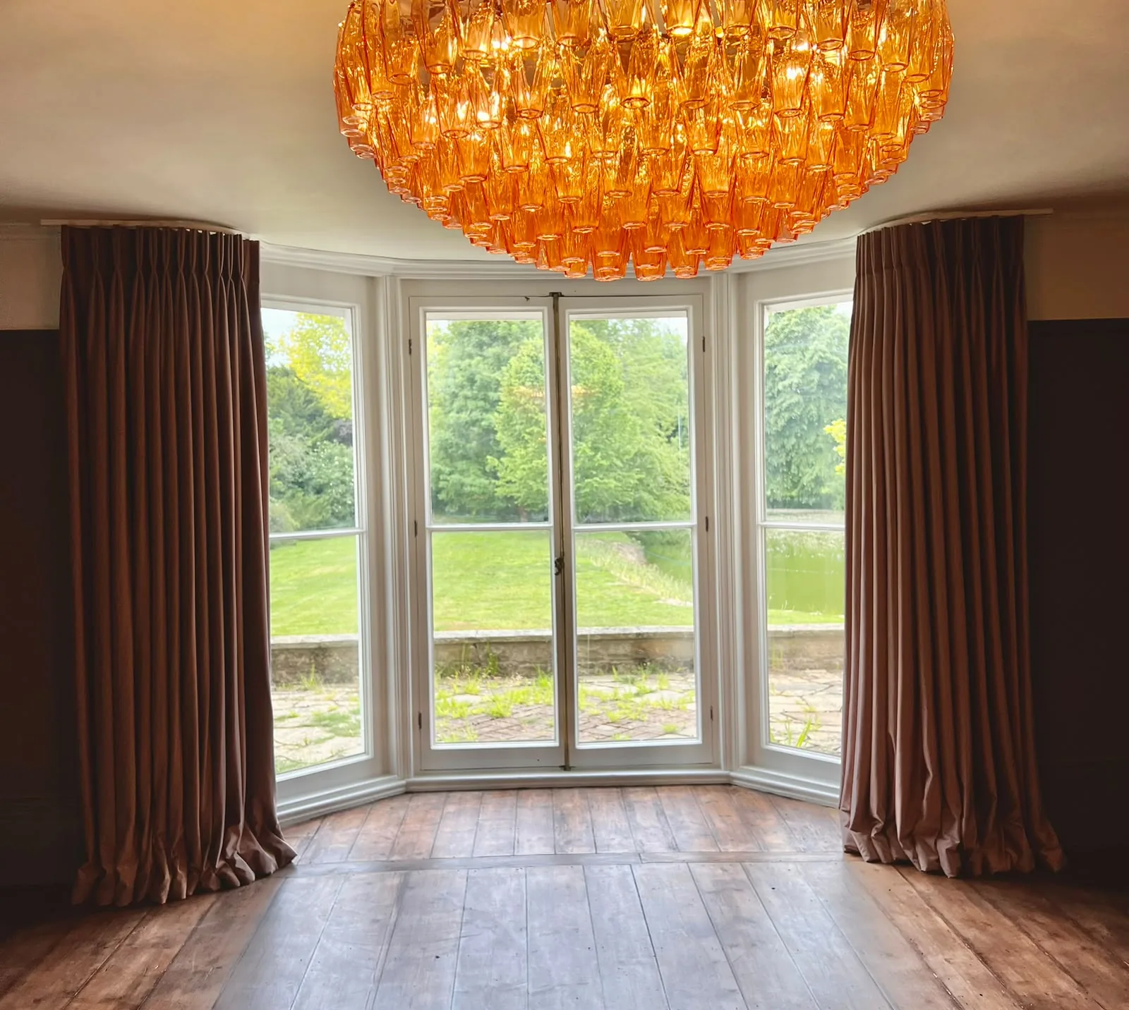 Plum curtains framing a bay of French windows beneath a large amber glass chandelier