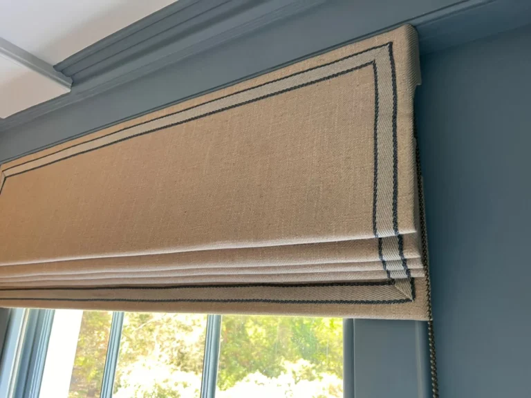 Natural Roman blind with a blue double-line border, fitted in a window recess on a blue wall