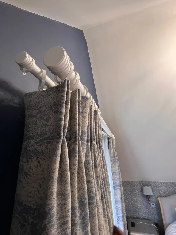 Looking up at a blue patterned curtain hung from a white wooden pole in a bedroom