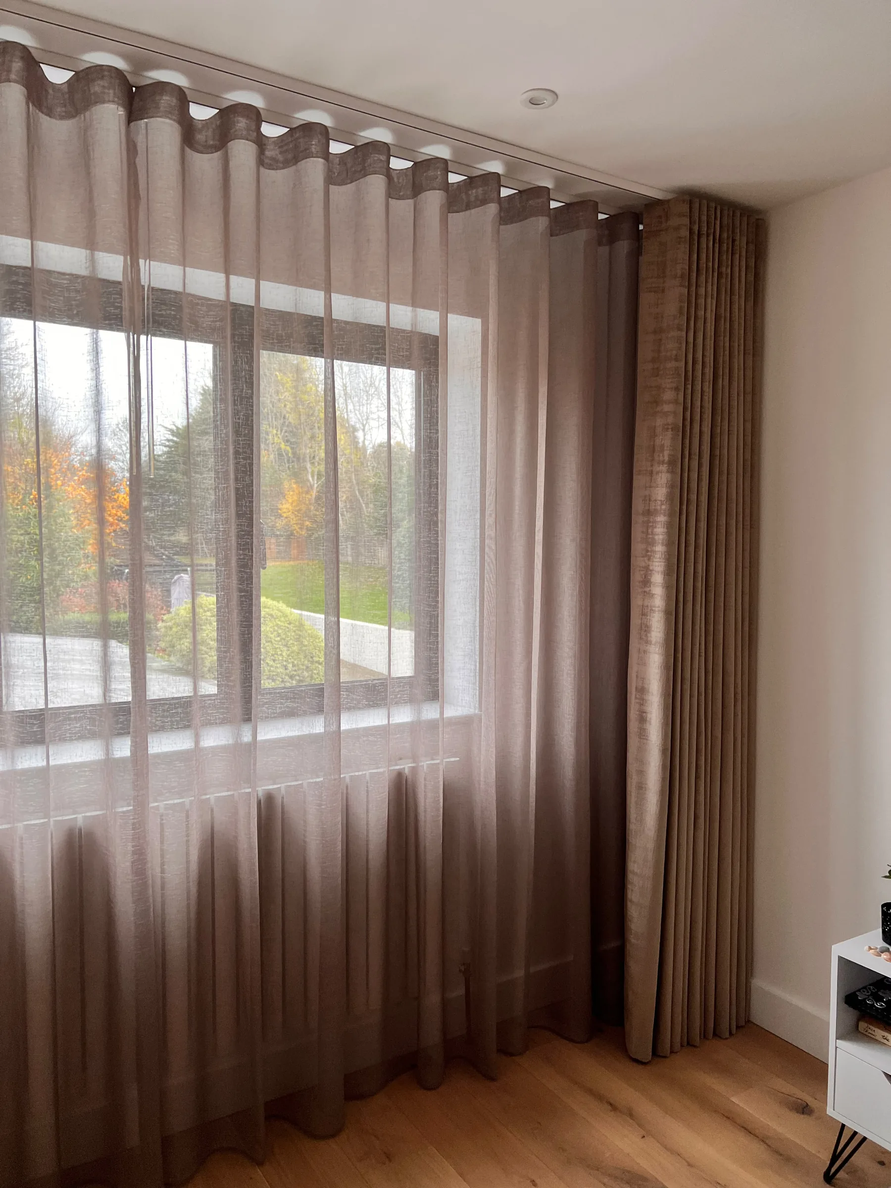 Taupe dress curtain and sheer wave voile at a bedroom window overlooking a garden