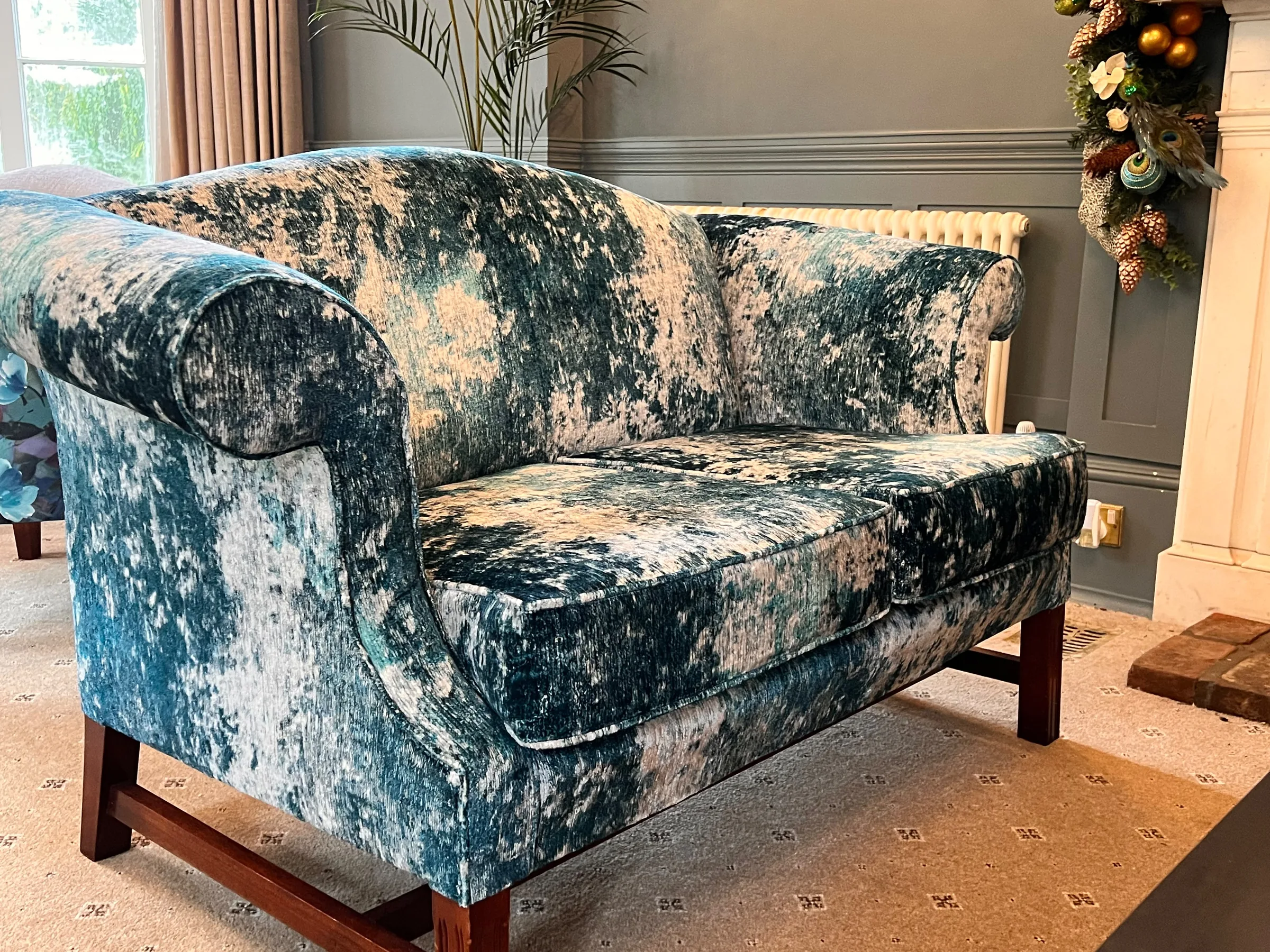 Camel-back sofa reupholstered in teal crushed velvet on mahogany legs, beside a fireplace
