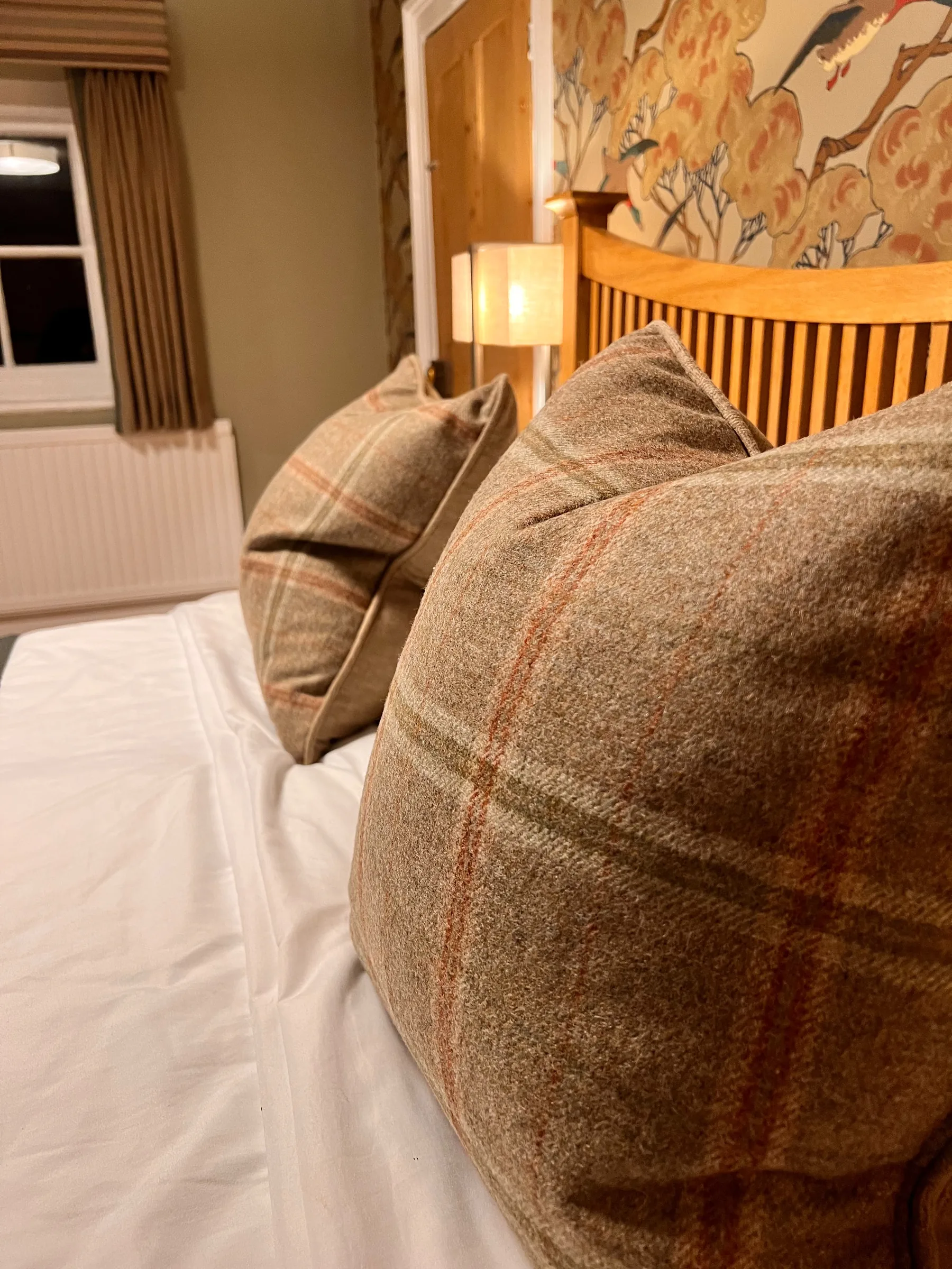 Close-up of tweed check cushions on a bed at Mulberry House, with bird and blossom wallpaper behind