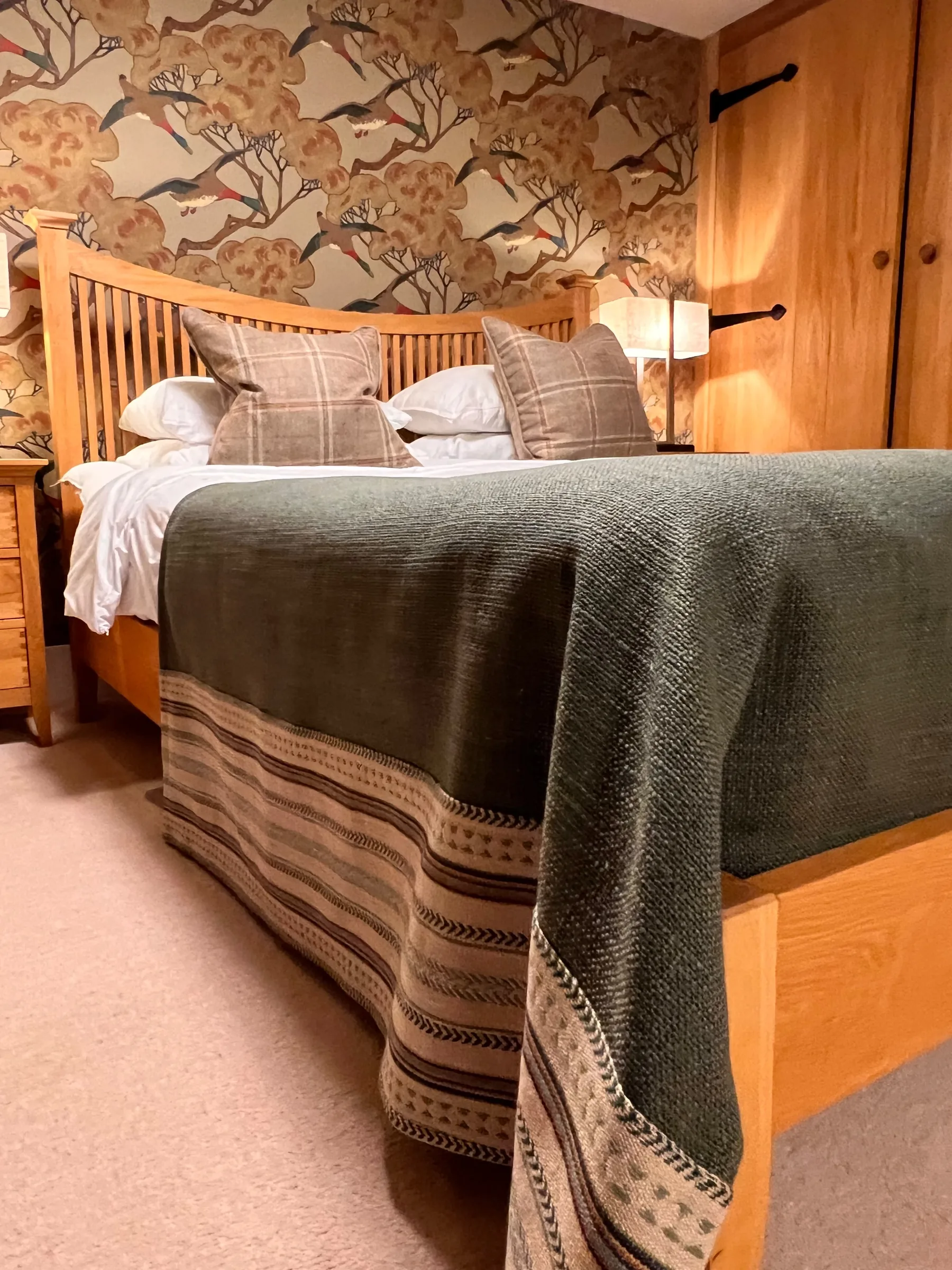 Oak bed at Mulberry House with a green throw with a striped border, check cushions and bird and blossom wallpaper