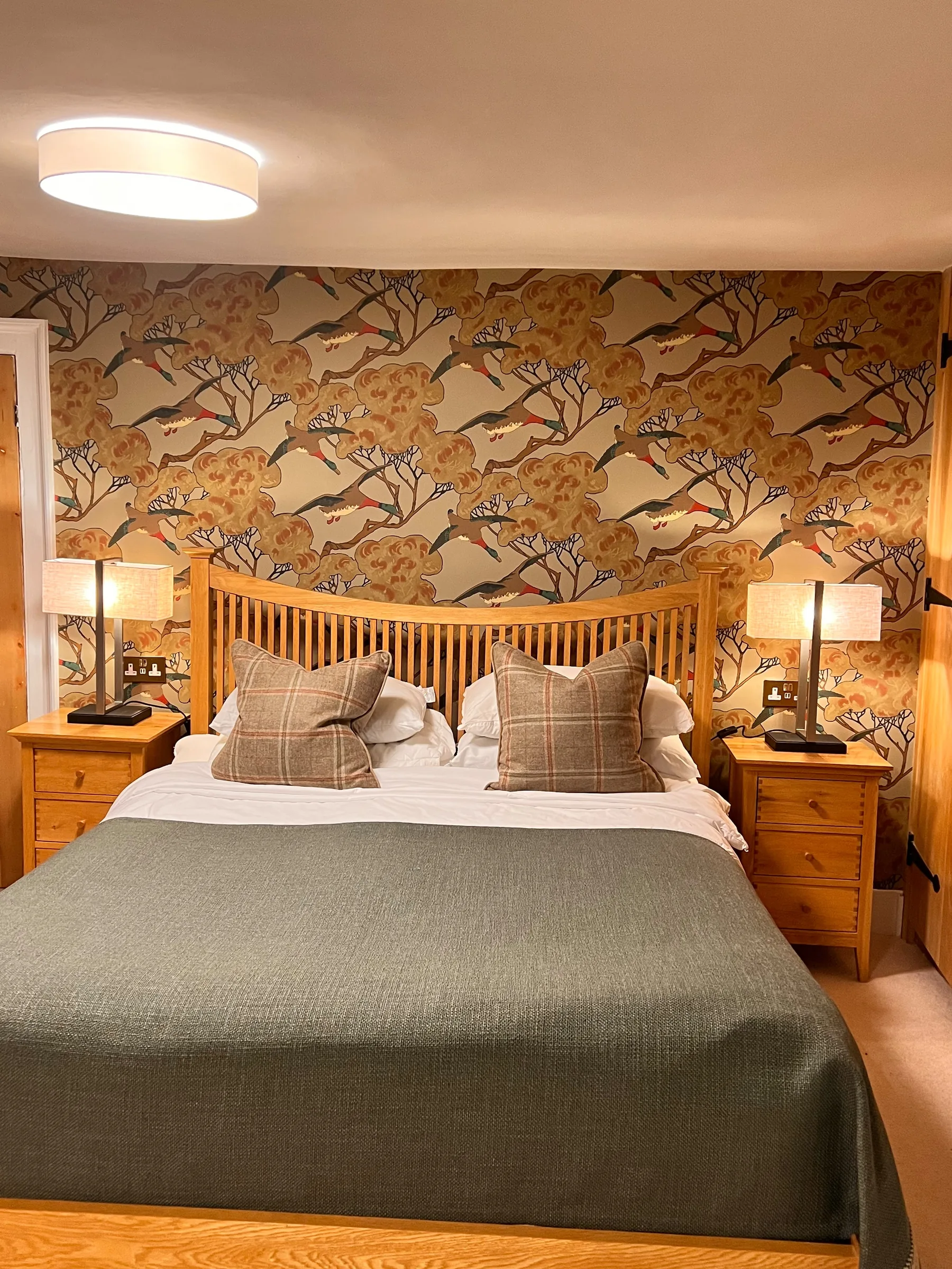 Oak bed at Mulberry House dressed with a green throw and check cushions between bedside lamps