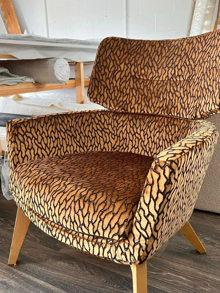 Mid-century style armchair upholstered in an amber and black animal-pattern velvet, in the workroom