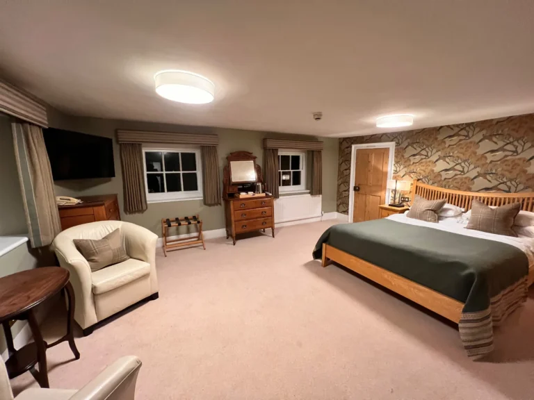 Bedroom at Mulberry House with striped pelmets over curtains, a cream tub chair and an oak bed with a green throw