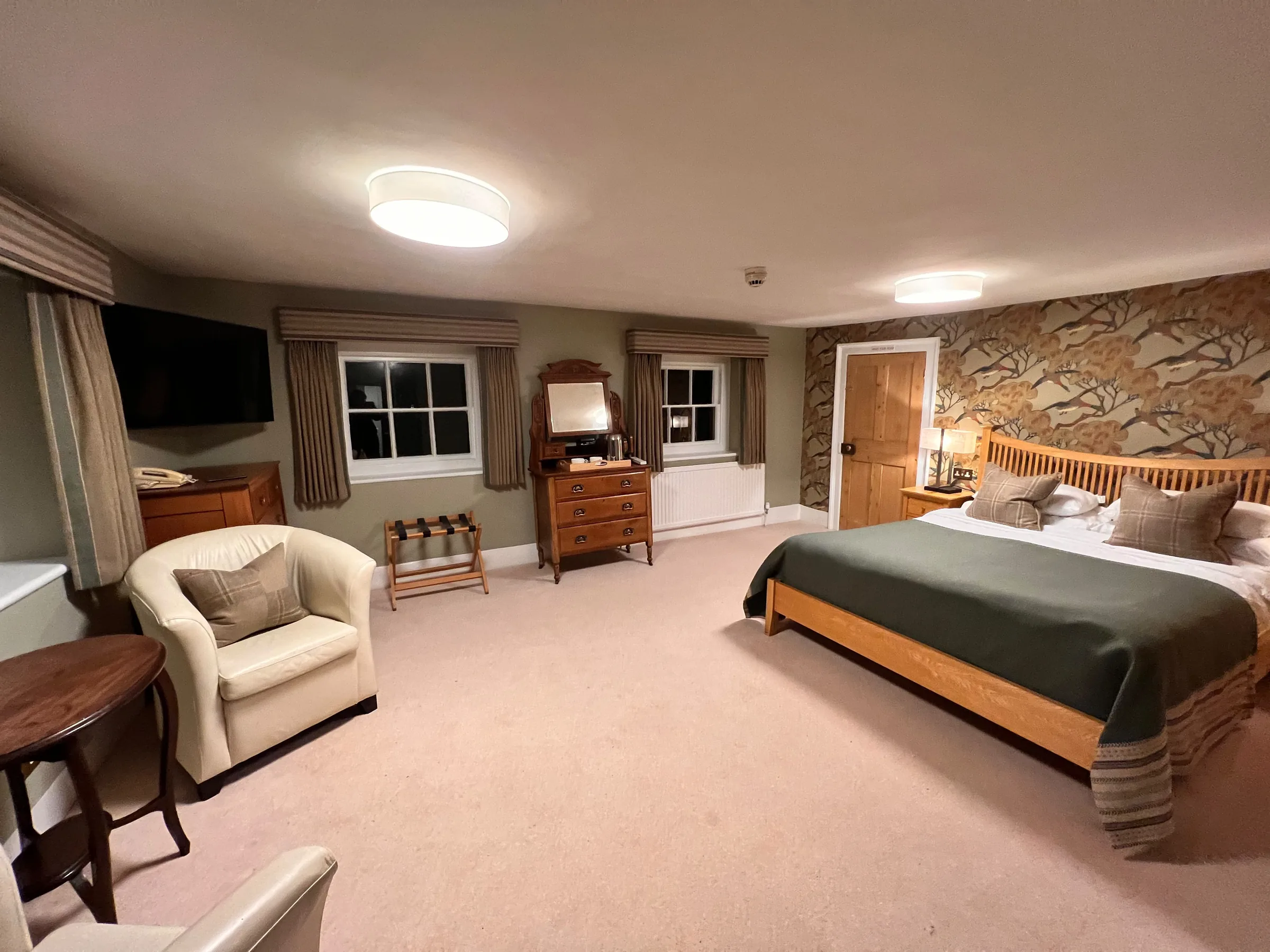Bedroom at Mulberry House with striped pelmets over curtains, a cream tub chair and an oak bed with a green throw