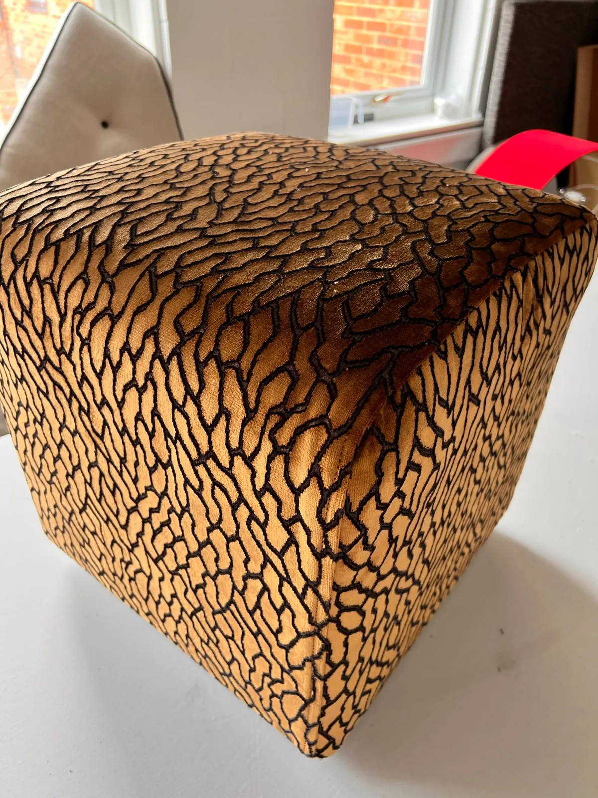 Close-up of a cube footstool in amber and black animal-pattern velvet