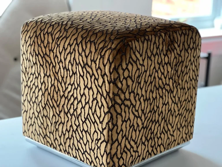 Cube footstool upholstered in amber and black animal-pattern velvet, on a white table in the workroom