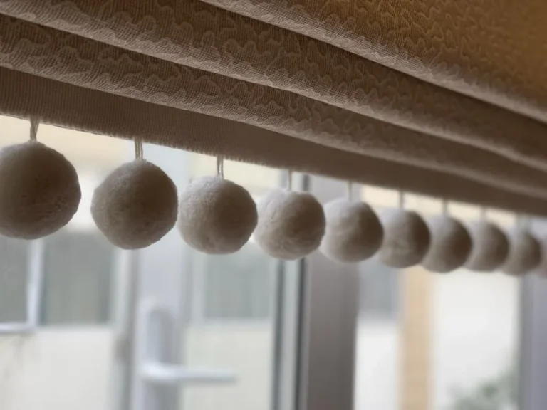 Close-up of a cream pom-pom trim along the edge of a blind
