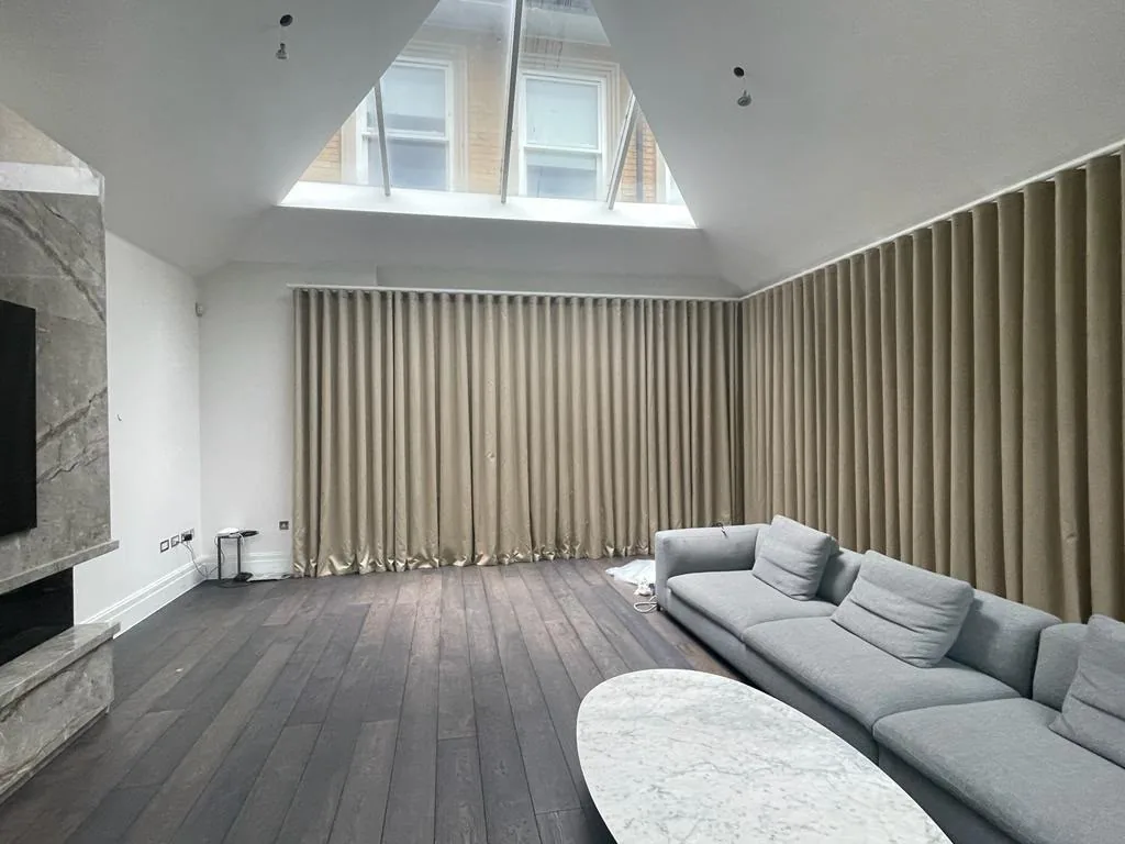 Vaulted living room with floor-to-ceiling neutral wave curtains along two walls and a grey corner sofa
