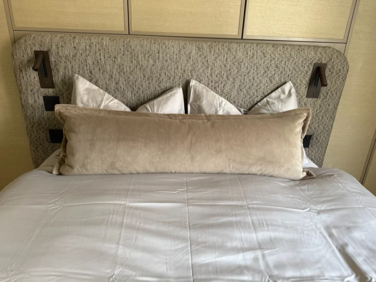 Bed with a textured woven upholstered headboard, built-in reading lights and a velvet bolster cushion