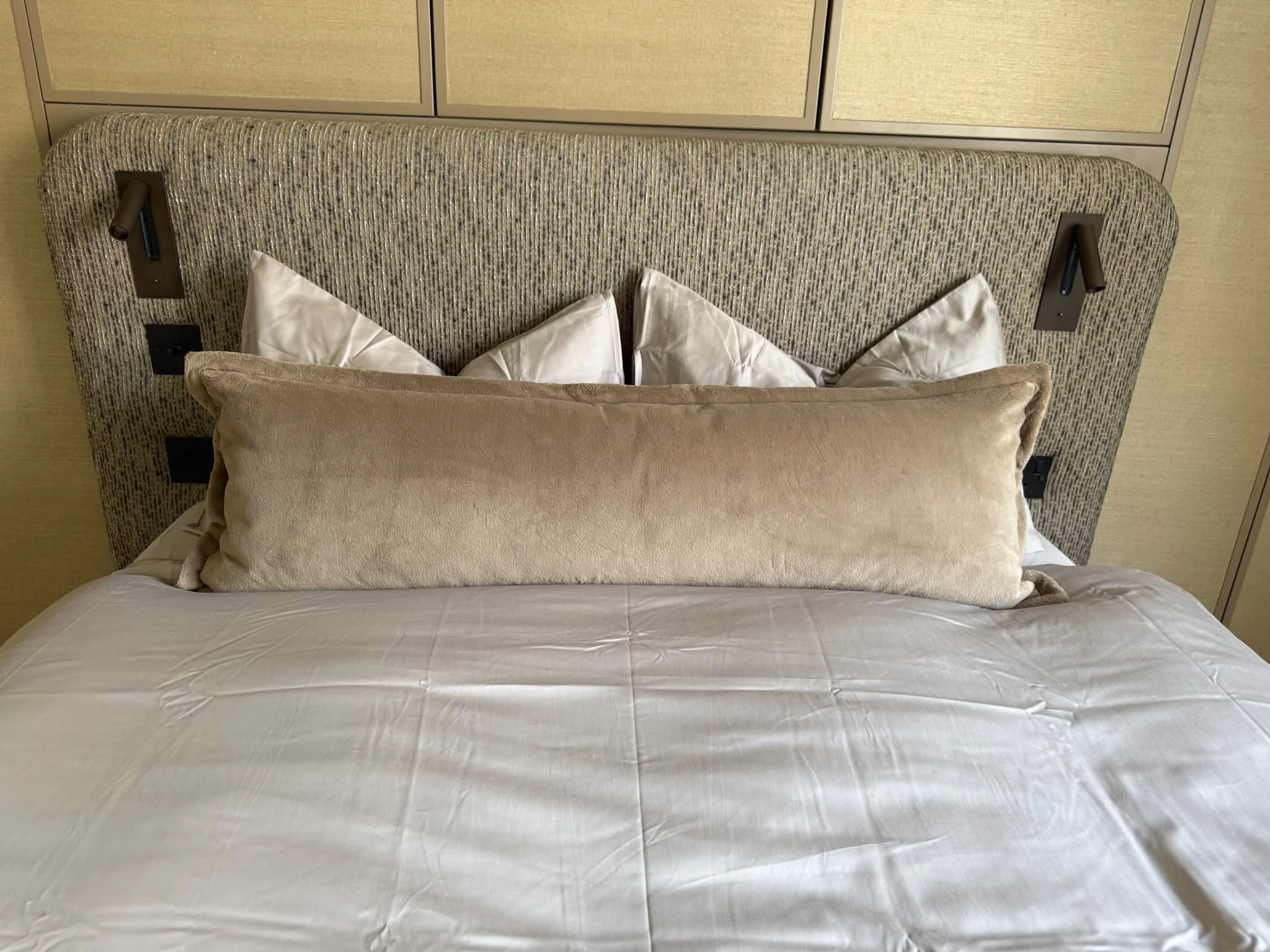 Bed with a textured woven upholstered headboard, built-in reading lights and a velvet bolster cushion