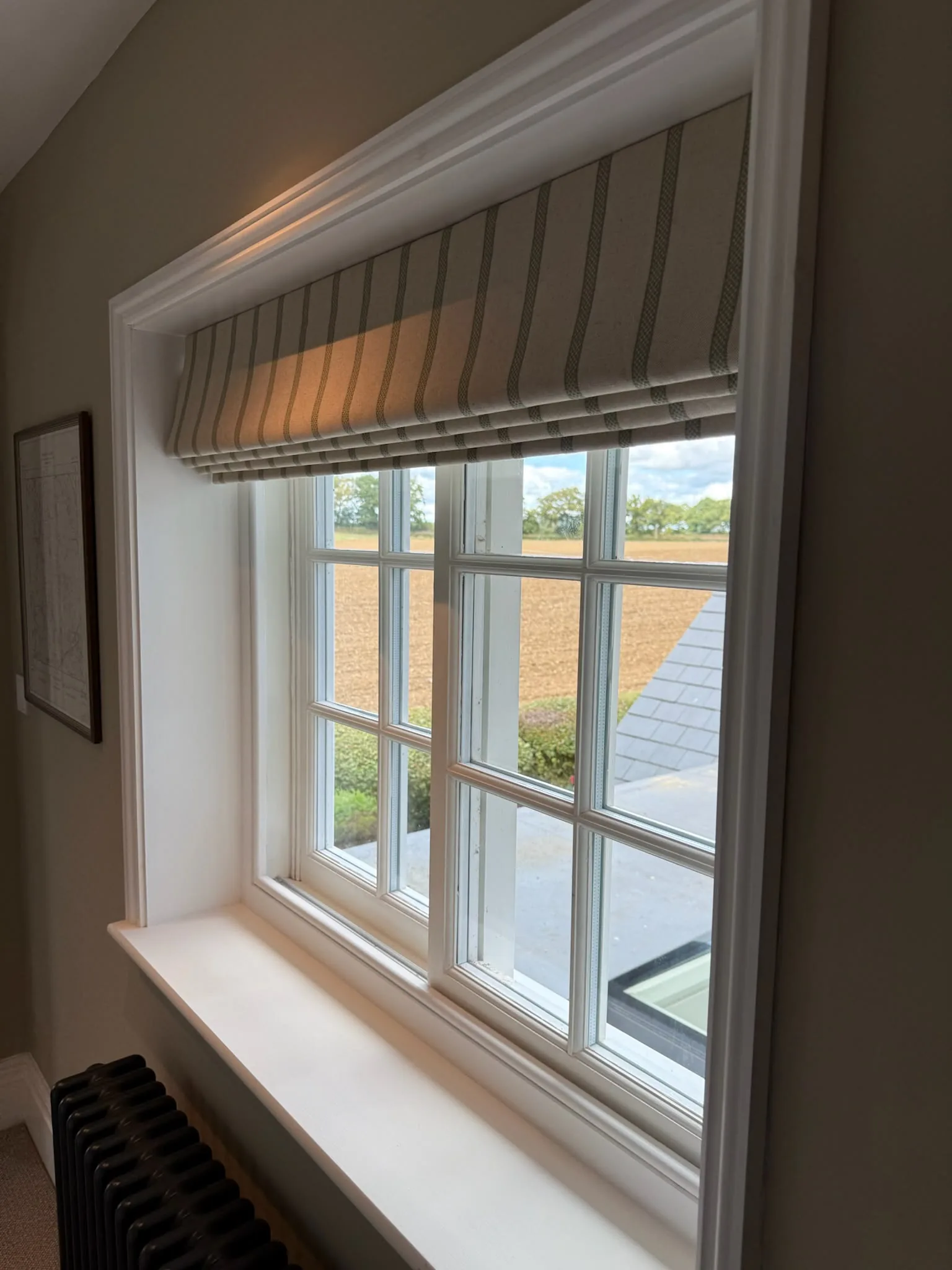 Striped Roman blind raised in a deep window reveal overlooking fields