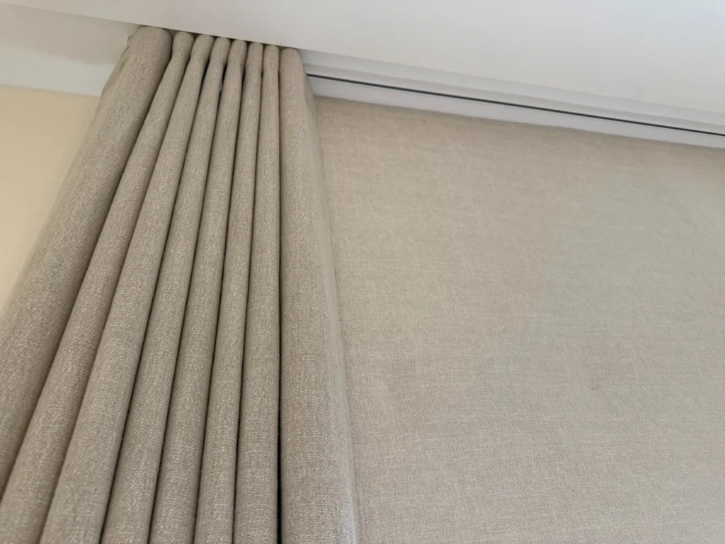 Looking up at the pleated heading of a neutral textured curtain on a ceiling track