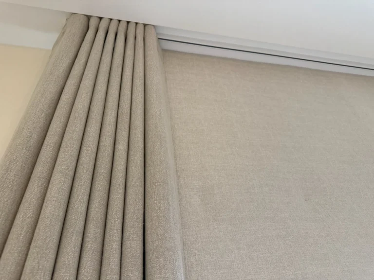 Looking up at the pleated heading of a neutral textured curtain on a ceiling track